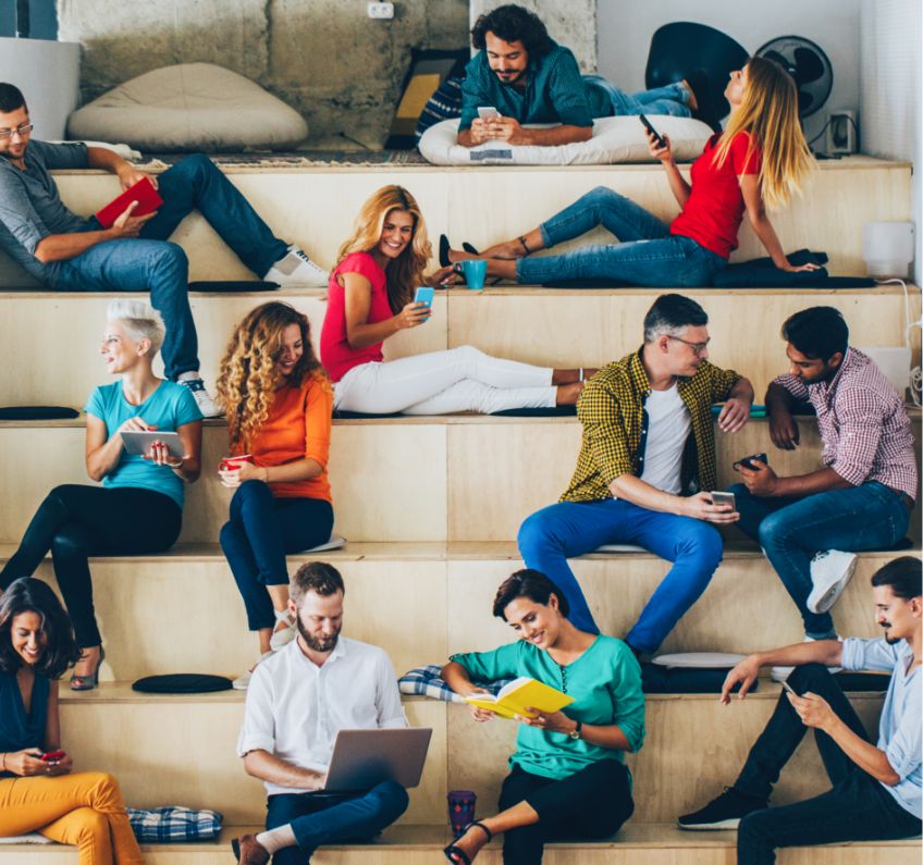 Gruppe von jungen Menschen sitzt auf verschiedenen Ebenen mit Laptop, Handy, Kaffeebecher zusammen