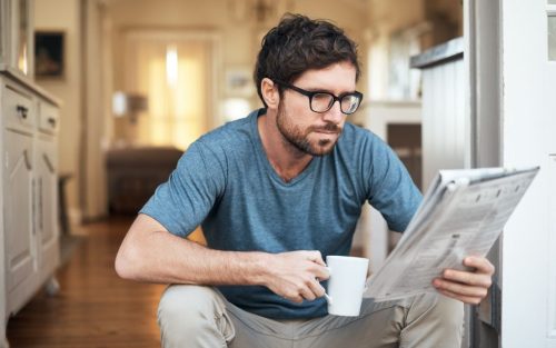 Mann mit Kaffeebecher sitzt auf Stufe und liest Zeitung, Bild symbolisiert Anzeigenblätter