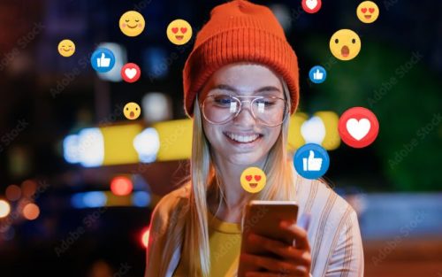 Social Media: Junge Frau mit Brille und Mütze schaut aufs Smartphone, um sie herum verschiedene Emojis