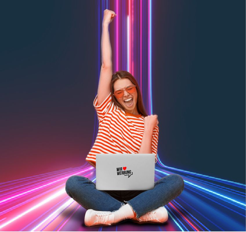 Junge Frau im Schneidersitz und Laptop mit Wir-lieben-Werbung-Sticker in Siegerpose