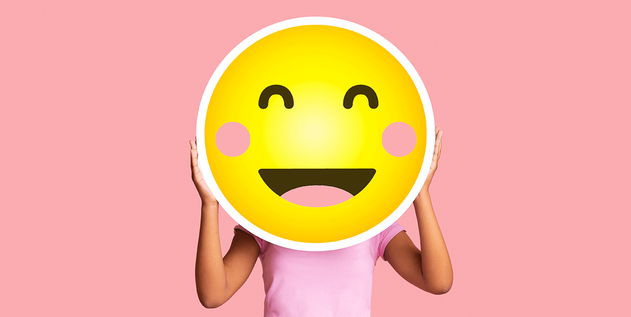 Person hält ein Bild von einem lachenden Emoji vor ihr Gesicht|Emoji Staunen überrascht|Emoji mit gefalteten Händen