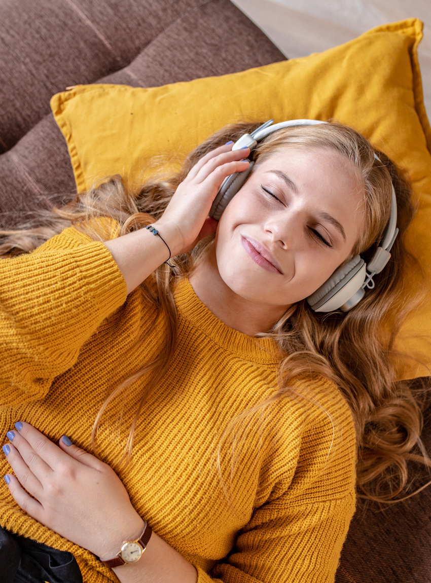 Frau mit Kopfhörern auf der Couch, die Musik genießt symbolisiert erfolgreiches Audio-Marketing.