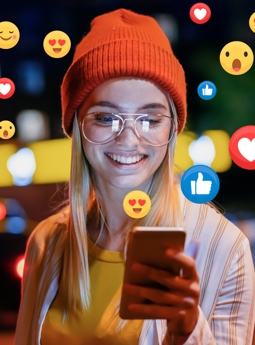 Junge Frau am Handy mit Emojis in der Luft symbolisieren Social Media Werbung