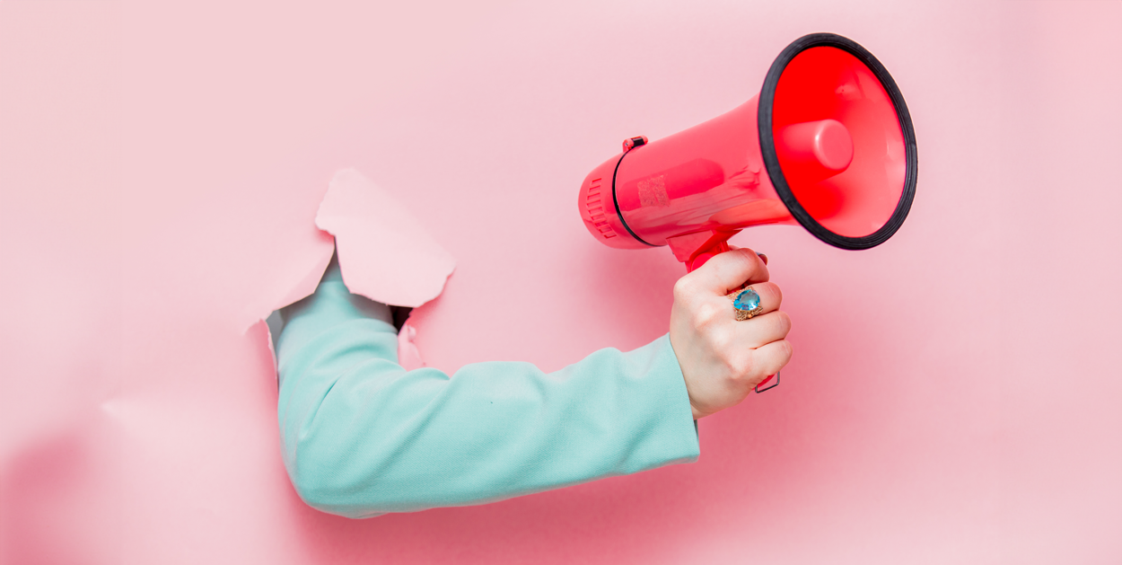 Hand durch die Wand mit Megaphone symbolisiert Krisenkommunikation von Unternehmen.